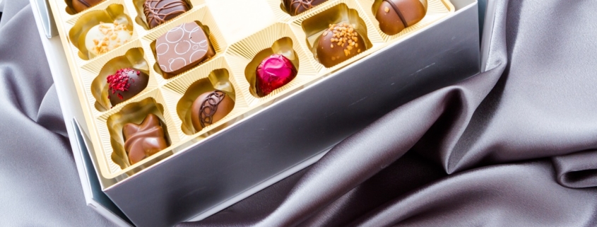 Geschenkbox mit verschiedenen Gourmet-Schokoladentrüffeln auf silbernem Seidenstoff.