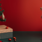 Table with gift and Christmas trees in decorations in front of red background